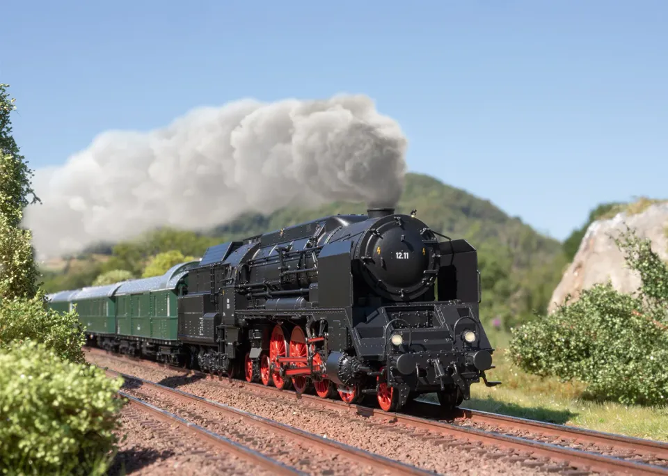 Die Märklin 12.11 zieht einen grünen Schnellzug durch eine Modellbahn-Landschaft, dabei steigt weißer Dampf auf
